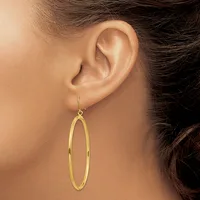 A person wearing a long, polished gold oval hoop earring hanging from their earlobe.