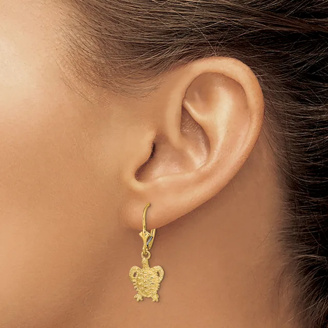 A gold-toned turtle charm earring hangs from a lever-back hook on a person's earlobe.