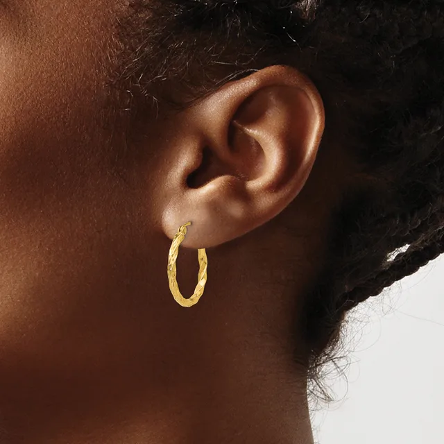 A person wearing textured gold hoop earrings is shown from the side, displaying the earrings against their ear and neck.