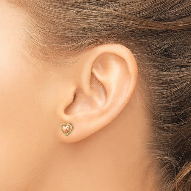 A small heart-shaped stud earring with a decorative border worn in the earlobe of a person with brown hair.