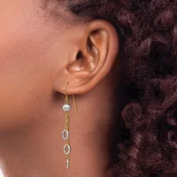 A person wearing a gold-toned drop earring with a small pearl bead at the top and three oval link charms hanging below.