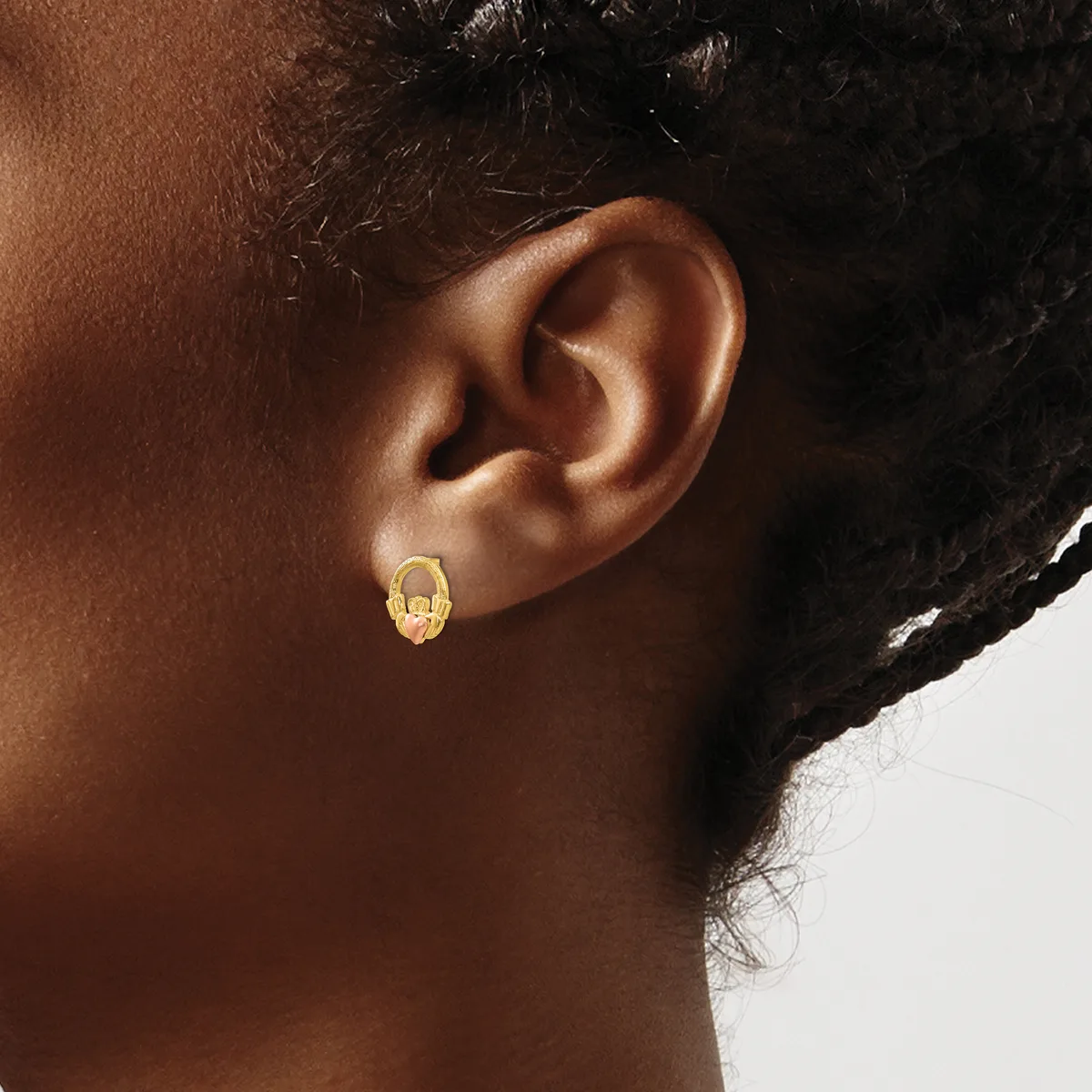 A person wearing a small gold hoop earring with a textured oval surface on their earlobe.