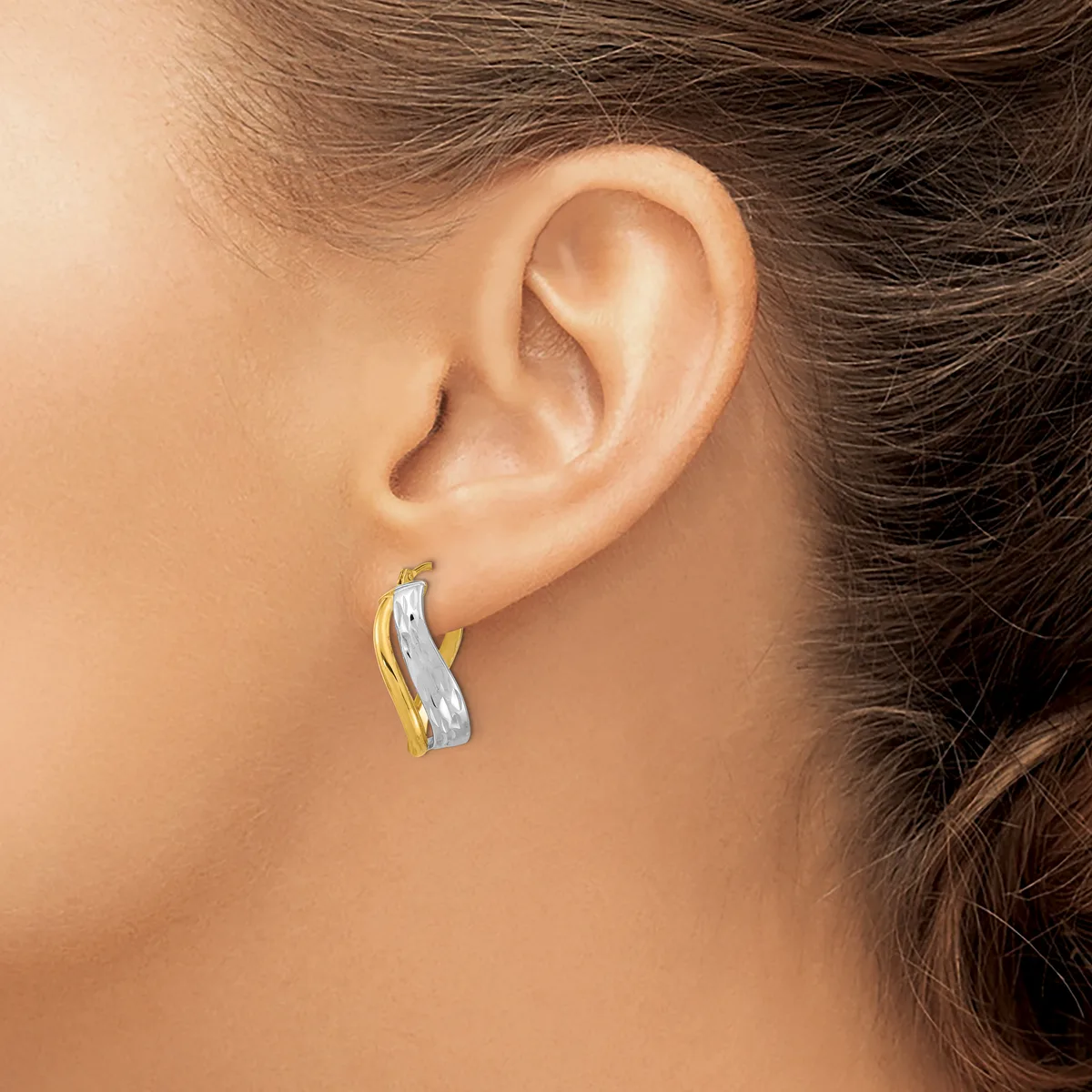 A person wearing a two-tone hoop earring with a textured surface, combining white and yellow metal, displayed on their earlobe.