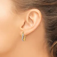 A person wearing small two-tone hoop earrings with a twisted or textured design, shown from the side view of their ear.