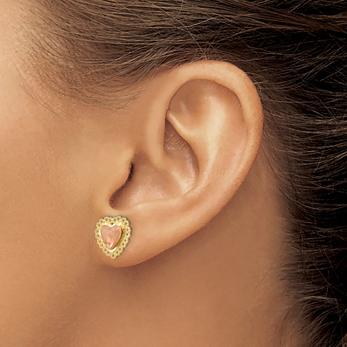 A person wearing a heart-shaped gold stud earring with a textured border, shown from the side view of their ear.