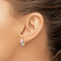 A person wearing a two-tone hoop earring with a textured white metal surface and polished yellow metal accent on the lower portion.
