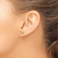 A person wearing a small gold stud earring in their earlobe, shown in profile against their ear and brown hair.