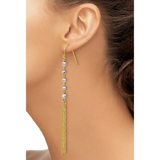 A woman wearing a long dangle earring with a gold-toned hook, small silver-colored beads strung along the upper portion, and a tassel of fine gold chain hanging below.