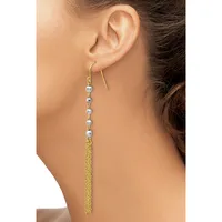 A woman wearing a long dangle earring with a gold-toned hook, small silver-colored beads strung along the upper portion, and a tassel of fine gold chain hanging below.