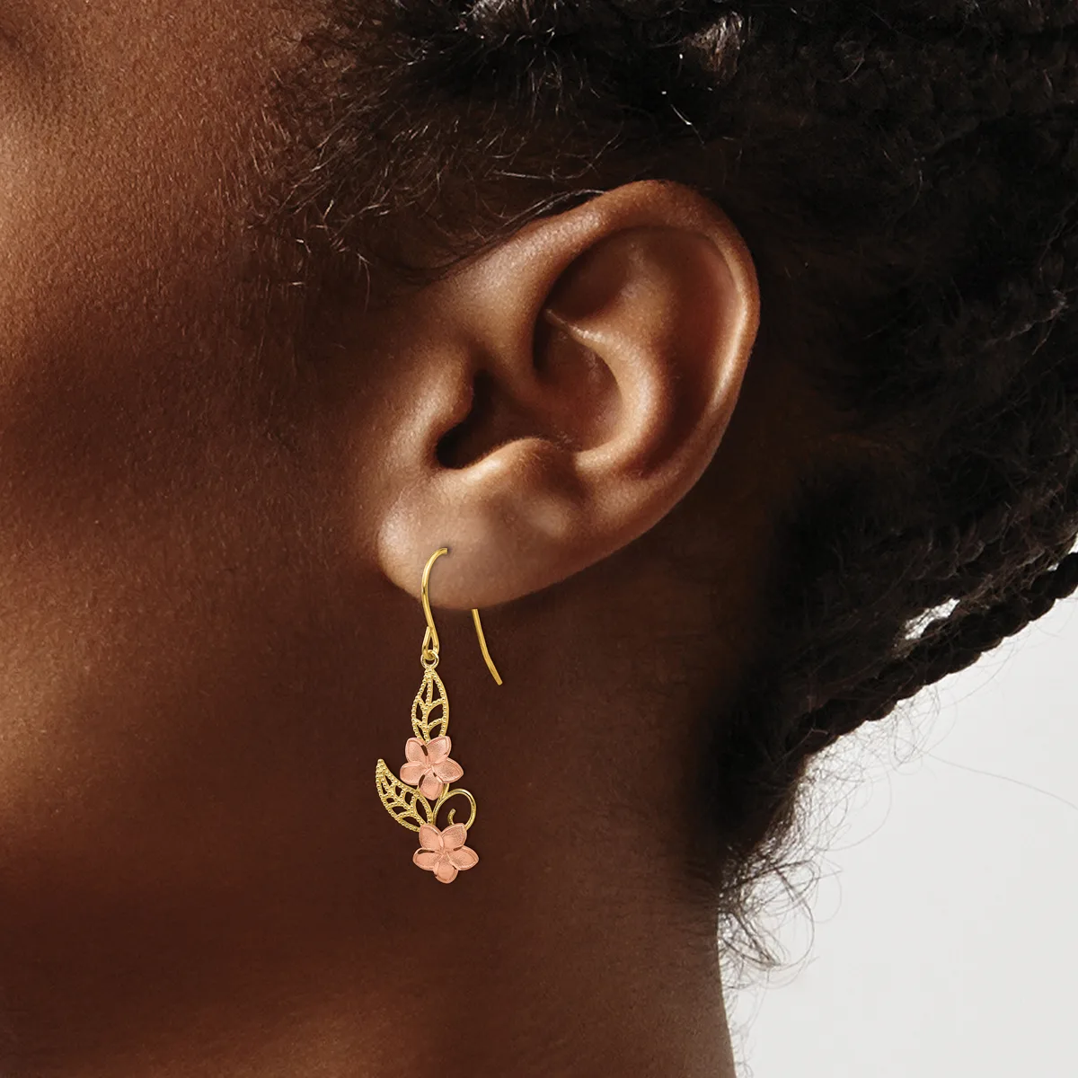 A person wearing gold drop earrings with leaf-shaped tops and clustered peach-colored stone pendants, shown from the side view of their ear and neck.