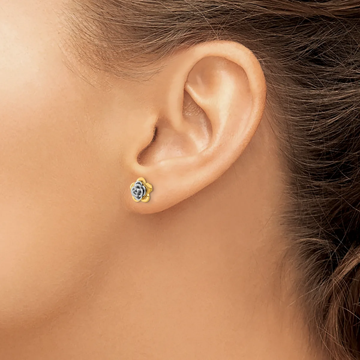 A person wearing a small decorative stud earring with a blue stone and gold-toned metal setting in their earlobe.