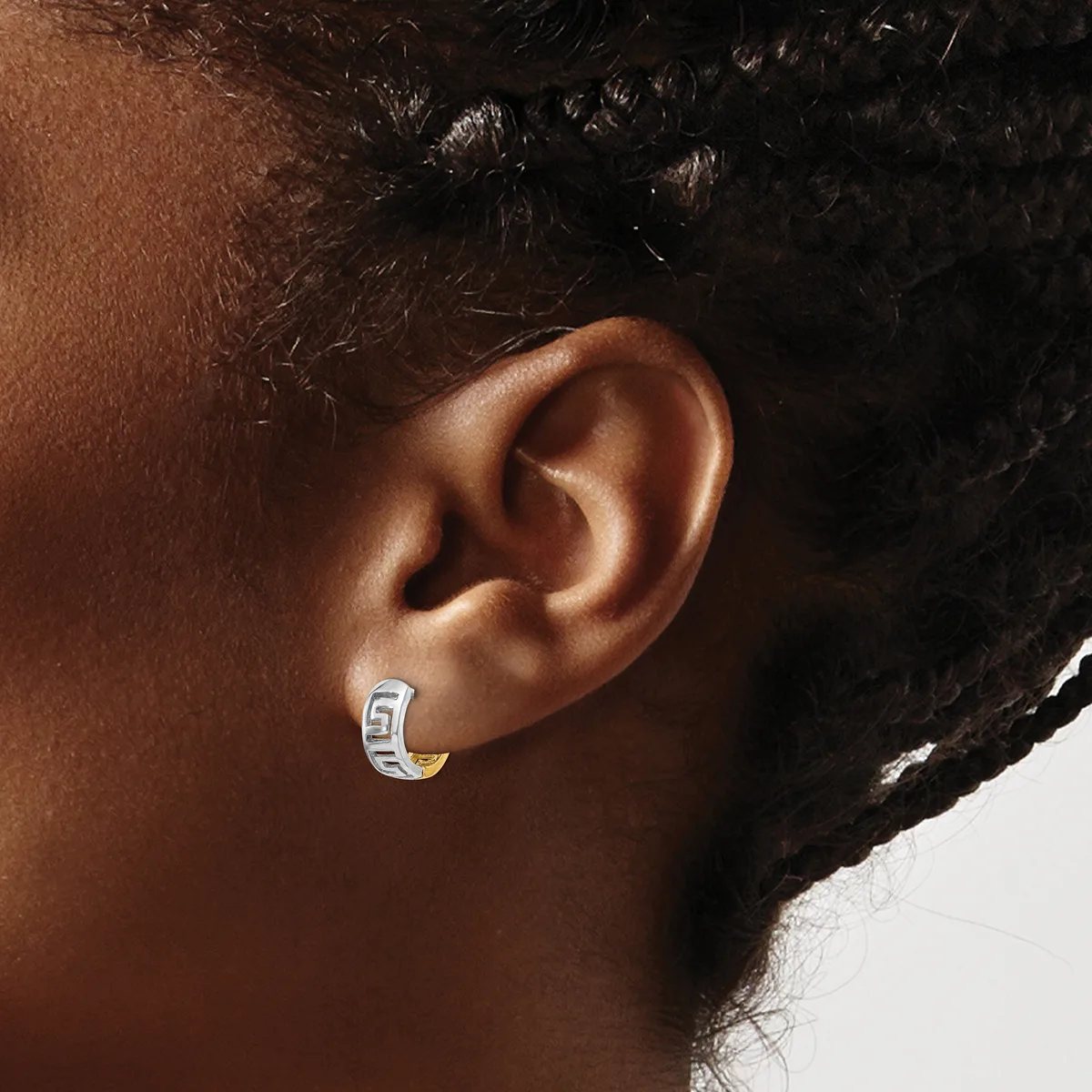 A small silver hoop earring with a geometric pattern worn on the earlobe of a person with medium brown skin tone and black curly hair.