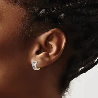 A small silver hoop earring with a geometric pattern worn on the earlobe of a person with medium brown skin tone and black curly hair.