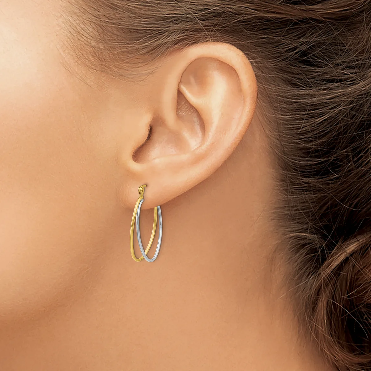 A person wearing two-tone oval hoop earrings with a polished finish, shown from the side against their ear.