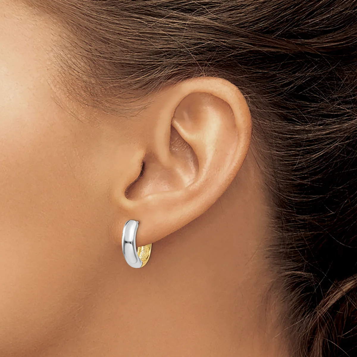 A person wearing a two-tone hoop earring with a white metal band and gold-colored accent on the lower portion, shown on their earlobe from a side profile view.