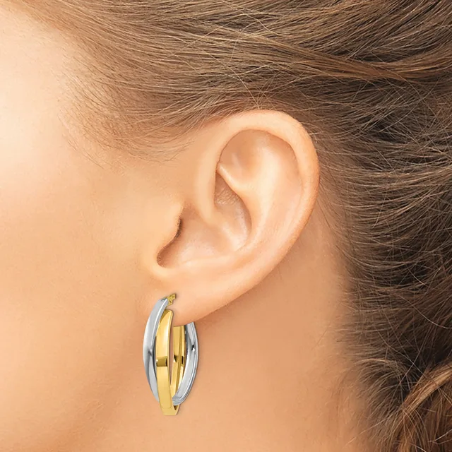 A person wears two-tone hoop earrings with alternating gold and silver curved bands, shown from the side view against their ear.