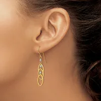 A woman wearing gold and silver interlocking oval drop earrings with fish hook closures, shown from the side profile against her ear.