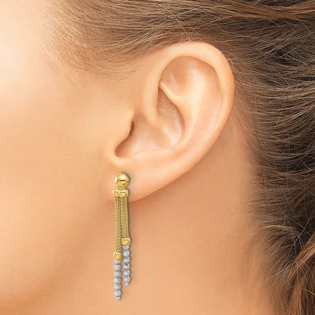 A woman wearing a long gold dangle earring with a textured mesh chain section and a strand of small round diamonds hanging from the bottom.