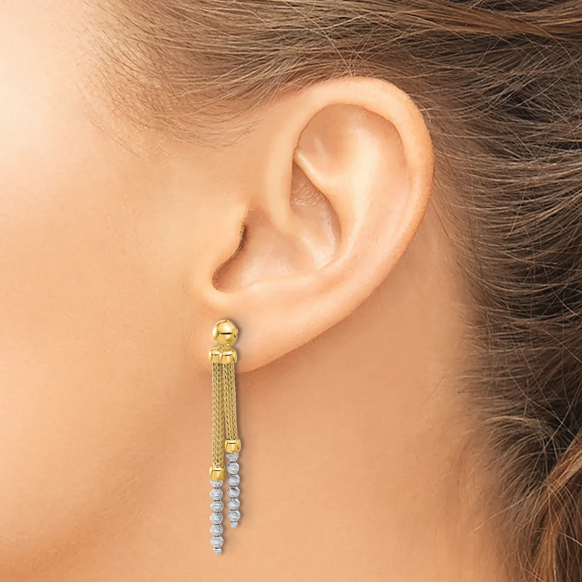 A woman wearing a long gold dangle earring with a textured mesh chain section and a strand of small round diamonds hanging from the bottom.