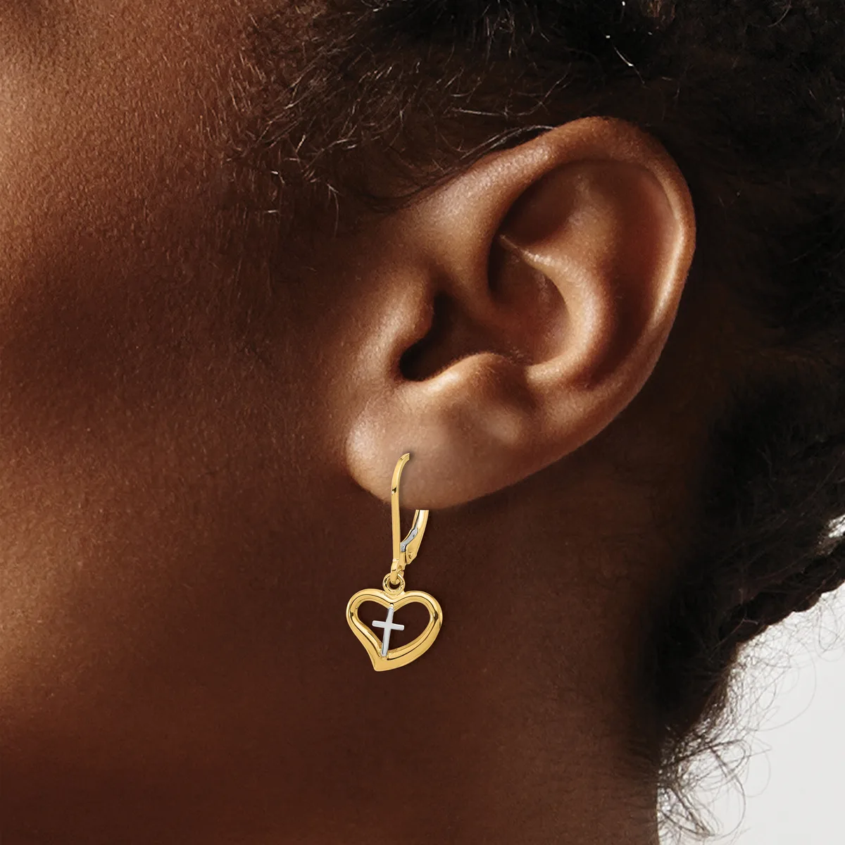 A person wearing a gold hoop earring with a small heart-shaped pendant hanging from it.