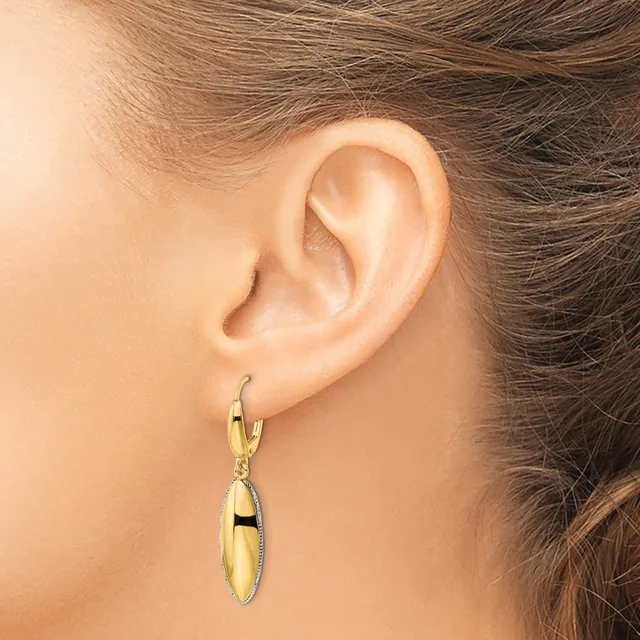 A person wearing a gold-toned oval dangle earring with a polished finish and textured border, shown from the side view against their ear.