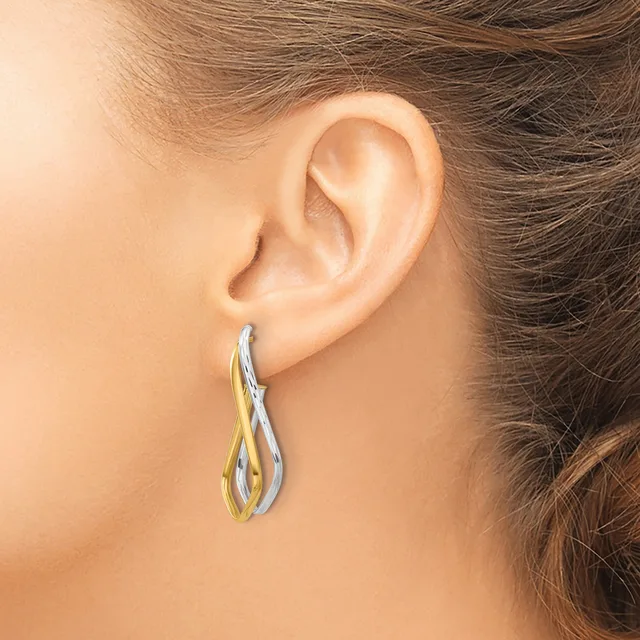 A woman wearing two-tone twisted drop earrings in gold and silver dangles from her earlobes.