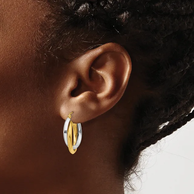 A person wearing two-tone hoop earrings with a gold center stripe and silver outer edges, shown from the side profile.