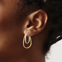 A person wearing two-tone oval hoop earrings with a gold outer band and silver inner band, shown from the side against their ear.