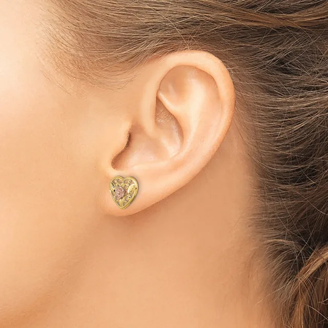 A person wearing a gold heart-shaped stud earring with pink and white gemstones, shown from the side view of their ear.