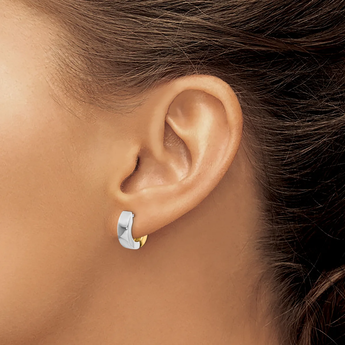 A person wearing a polished silver chunky hoop earring in their earlobe, shown in profile against their bare shoulder and neck.