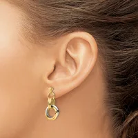A woman wearing a two-tone gold and silver dangling earring with interlocking circular rings hangs from her earlobe.
