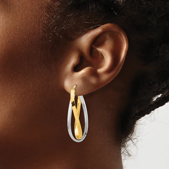A person wearing two-toned hoop earrings with white and gold-colored metal in a twisted or crossed design.