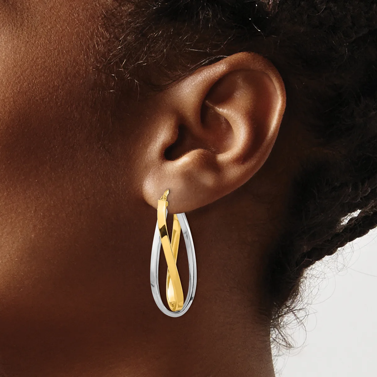 A person wearing two-toned hoop earrings with white and gold-colored metal in a twisted or crossed design.