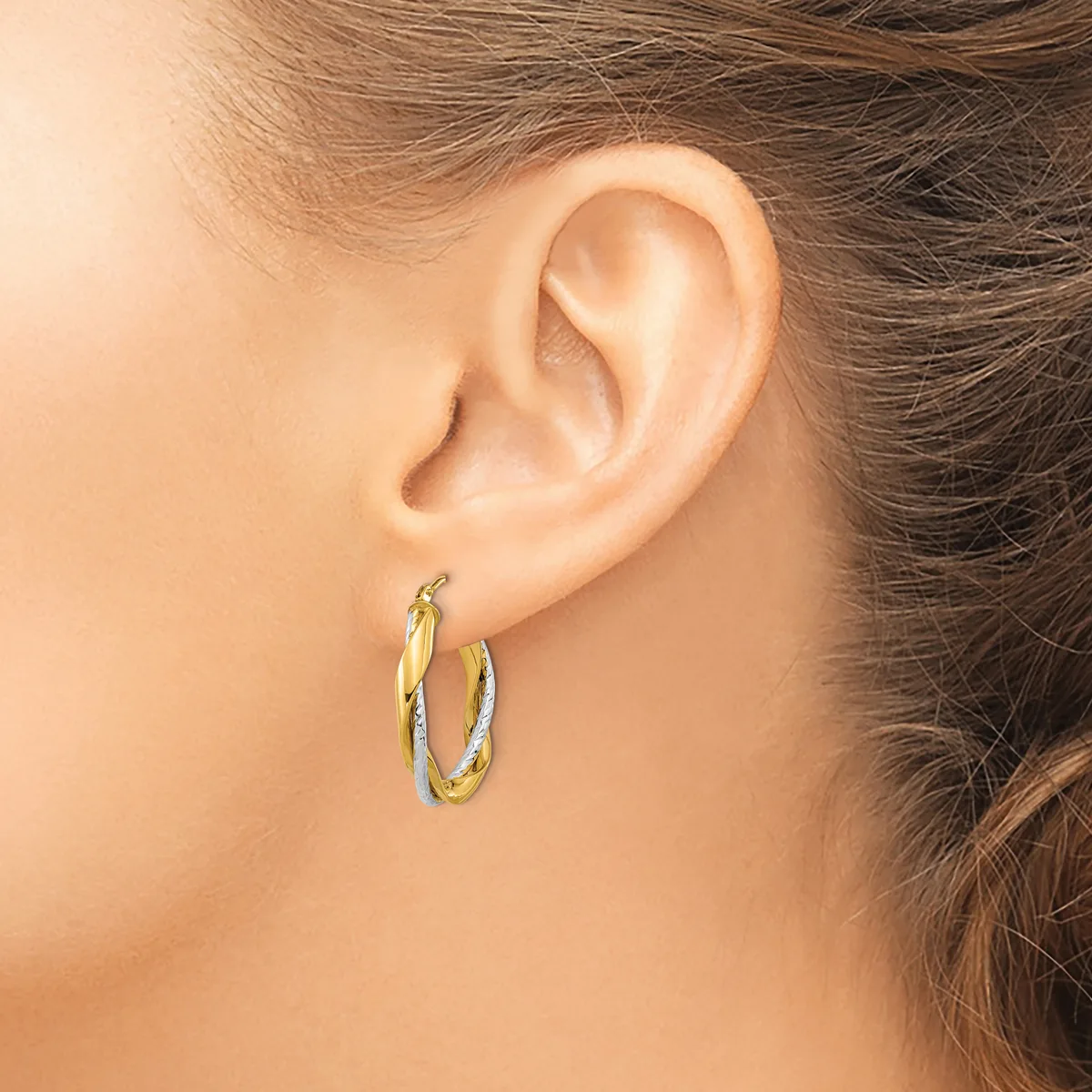 A person wearing two-tone gold hoop earrings with a textured surface, shown from the side view of their ear and neck.