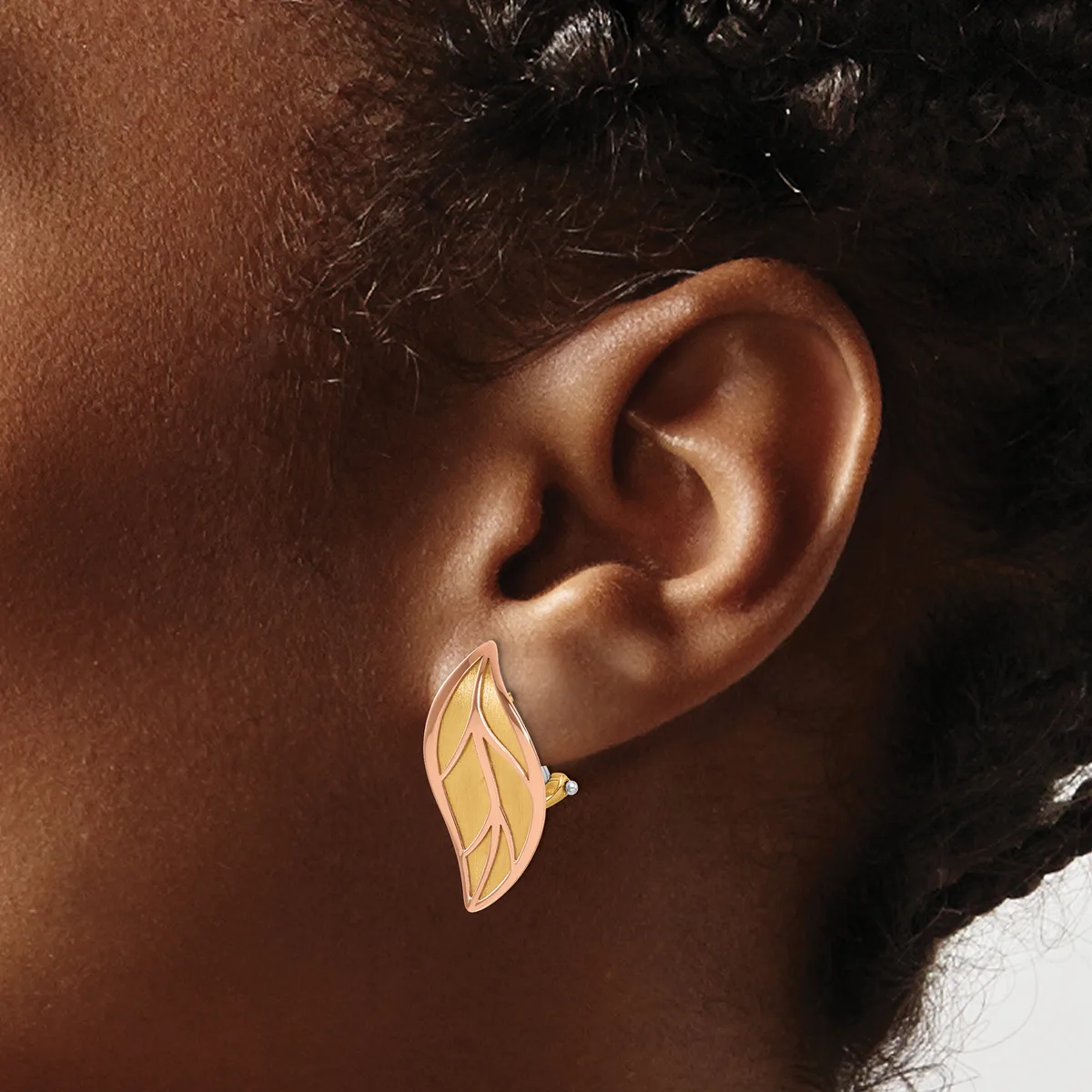 A person wearing a gold leaf-shaped earring with linear details and a small stone accent, shown from the side against their ear.