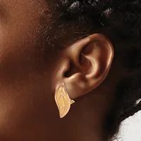 A person wearing a gold leaf-shaped earring with linear details and a small stone accent, shown from the side against their ear.