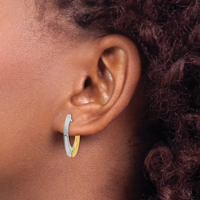 A two-tone hoop earring with silver and gold sections worn on the earlobe of a person with dark curly hair.