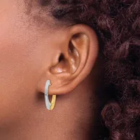 A two-tone hoop earring with silver and gold sections worn on the earlobe of a person with dark curly hair.
