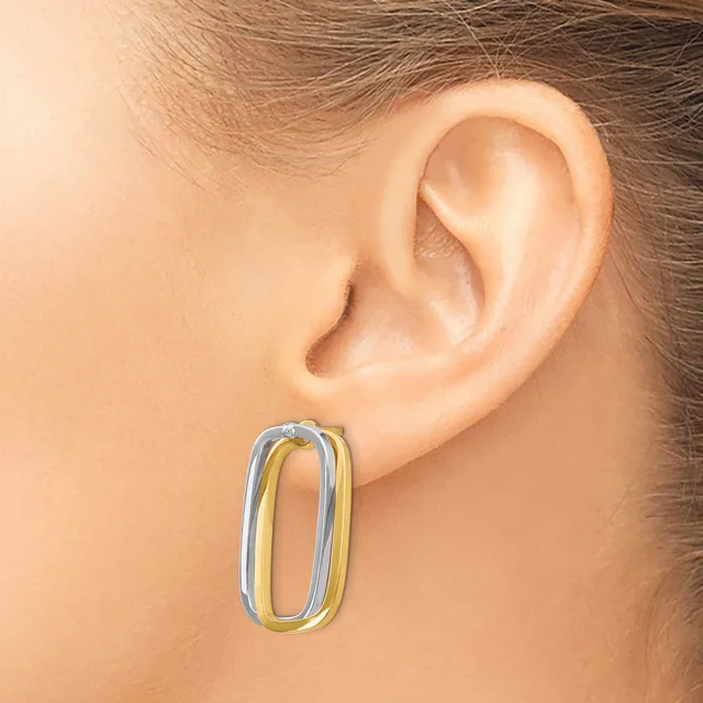 A two-tone oval hoop earring in white and yellow metal worn on a person's earlobe.