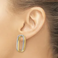 A person wearing a two-tone oval hoop earring in silver and gold metal, shown on their earlobe from the side.