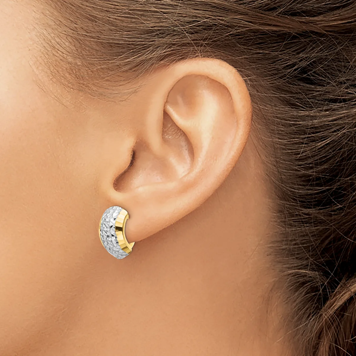 A chunky curved earring with a textured hammered finish in white metal and polished gold sections, worn on a model's earlobe.