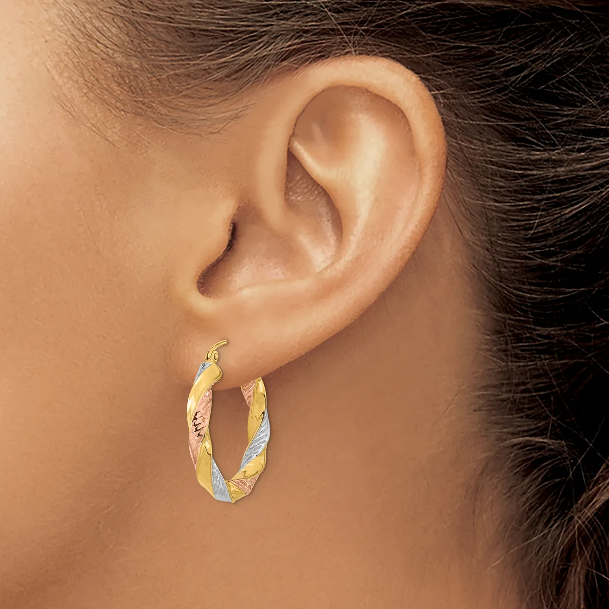 A person wearing a twisted gold hoop earring in their earlobe, shown in profile against their neck and shoulder.