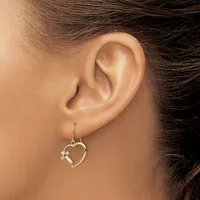 A person wearing a gold-toned heart-shaped dangle earring with a small diamond or crystal accent, shown from the side profile of their ear.