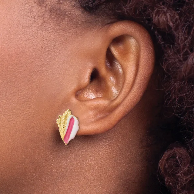 A person wearing a gold and pink enamel stud earring shaped like a leaf or feather, shown in profile view.