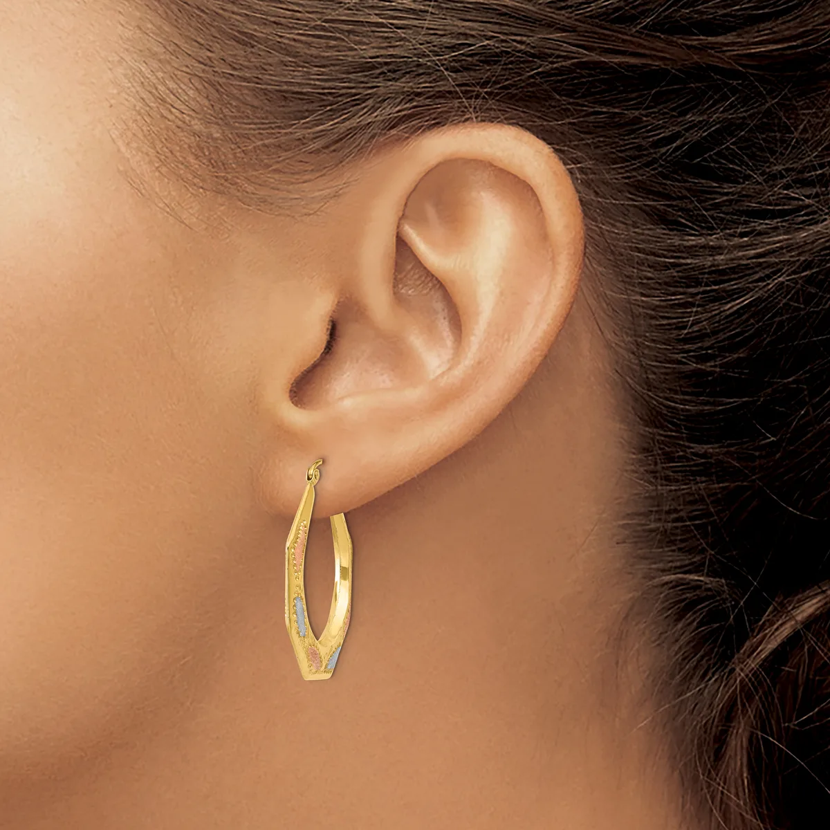 A person wearing gold oval hoop earrings with a textured finish, shown from the side profile displaying the ear and earrings.