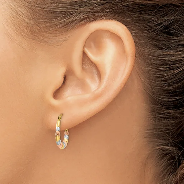 A close-up view of a person's ear wearing a two-tone gold and silver hoop earring with a textured surface.