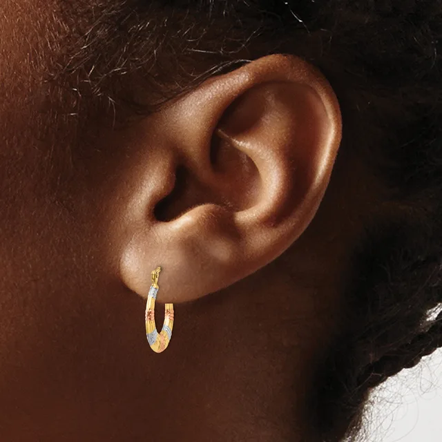 A close-up view of a person's ear wearing a pair of two-tone gold and silver textured hoop earrings.