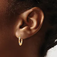 A close-up view of a person's ear wearing a pair of two-tone gold and silver textured hoop earrings.