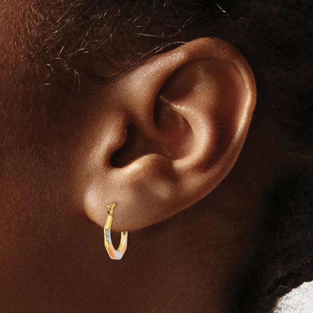 A gold hoop earring worn in the earlobe of a person with brown skin and dark hair, shown in profile against a dark background.