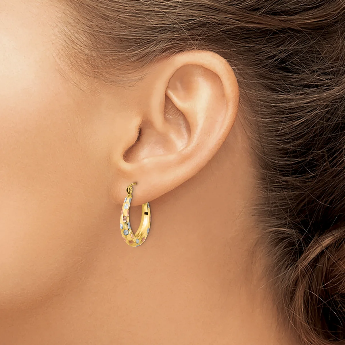 A person wearing gold hoop earrings with multicolored gemstone accents, shown from the side profile against their ear and neck.